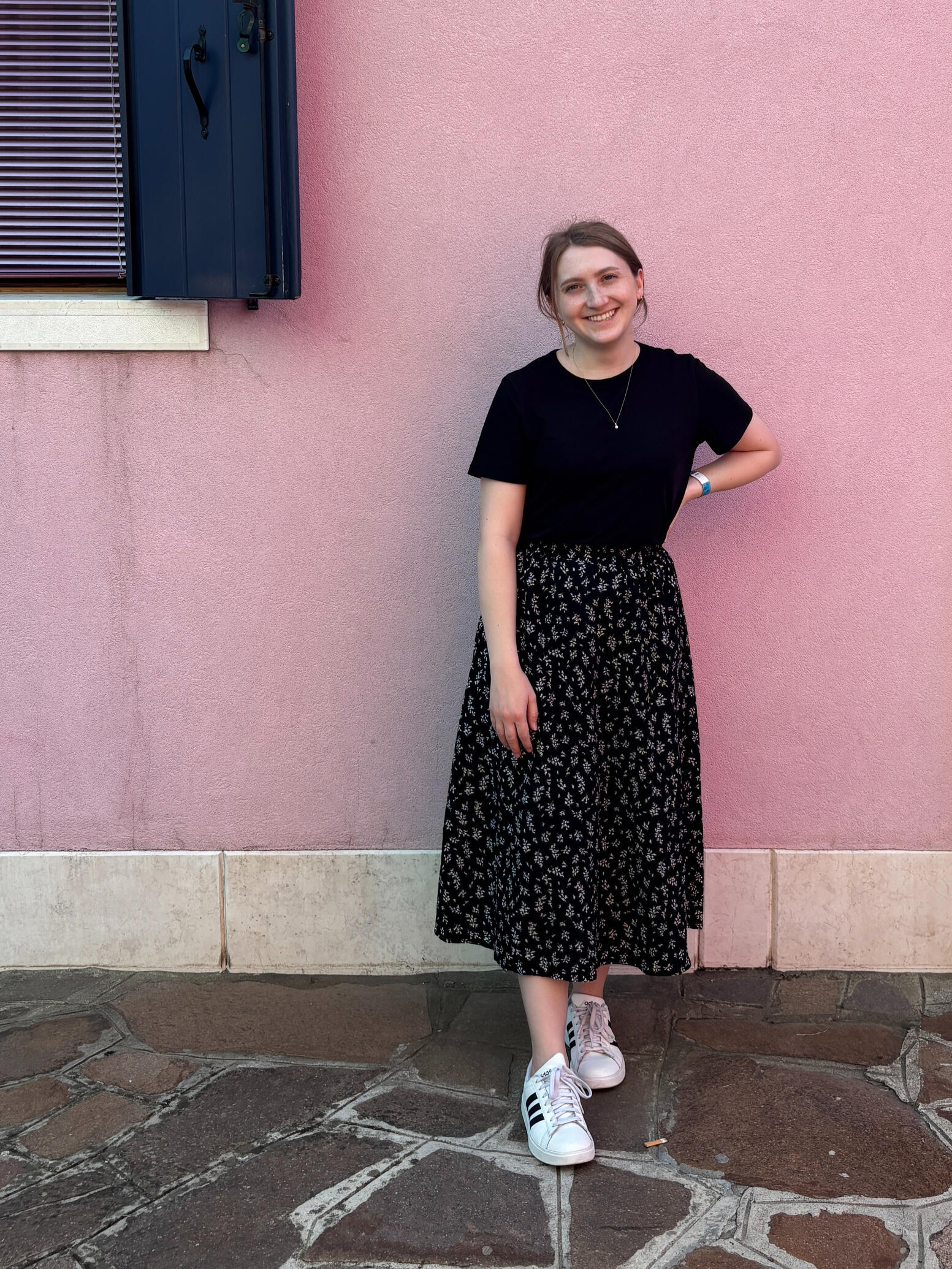 Amanda smiling in a black shirt and skirt in front of a pink building.